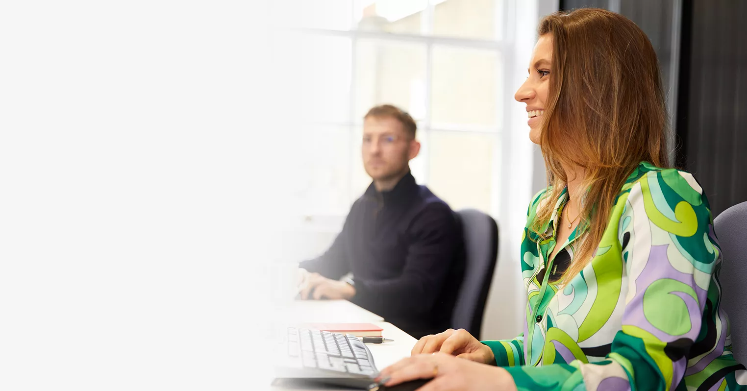 A woman at a desk, with an out-of-focus man in the background
