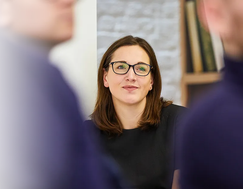 A woman in glasses between two out-of-focus people