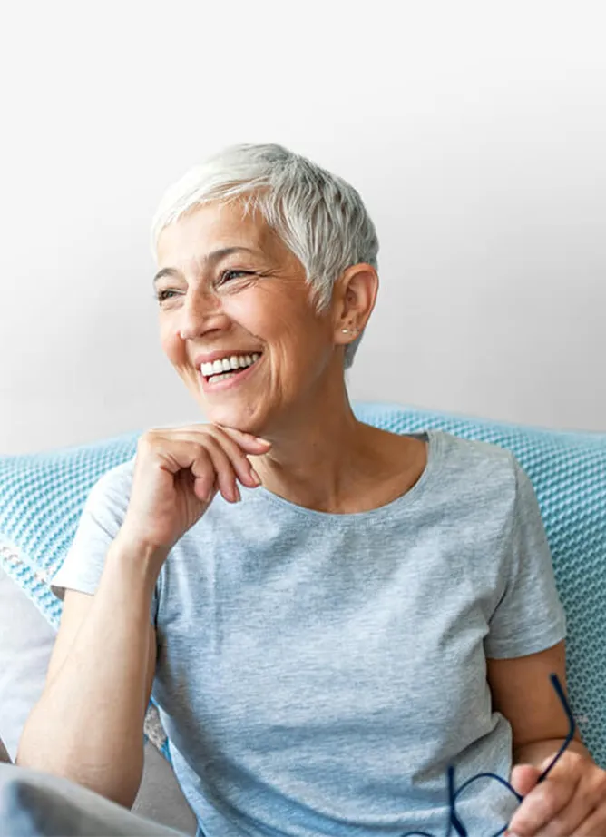 A woman sitting on a chair, she's holding her glasses in her hand and laughing