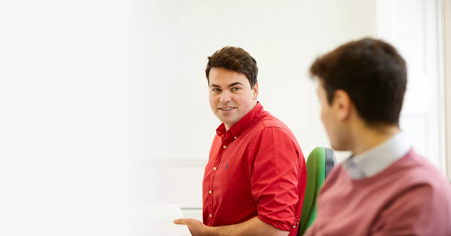 A man in a red shirt looks at an out of focus man in a pink jumper