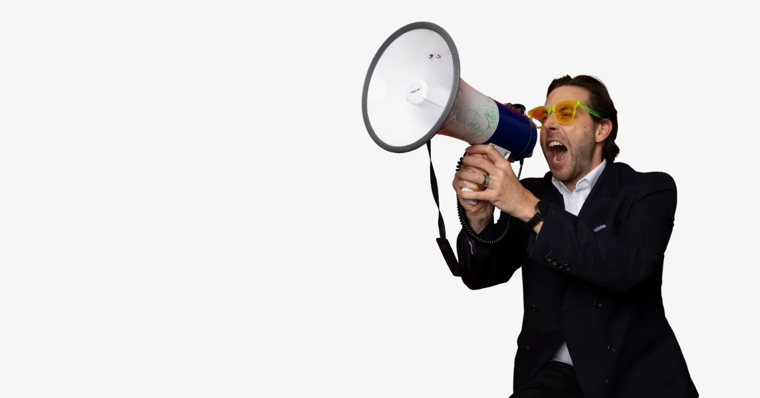Man wearing a suit ang glasses, shouting into a megaphone.